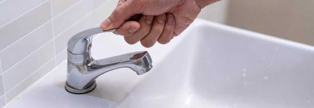 Hand dreht einen Wasserhahn auf.